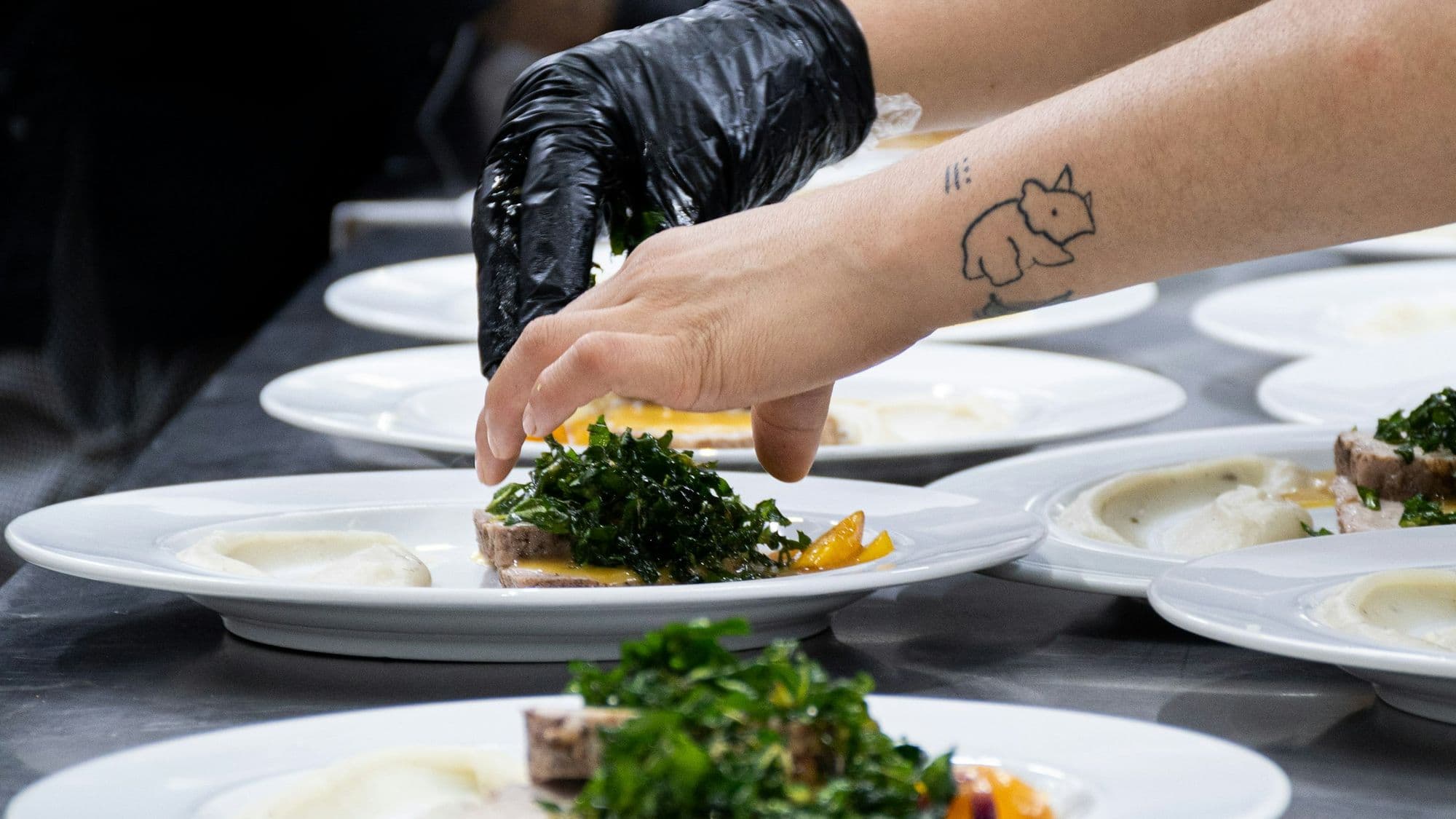 Gloved kitchen staff plating rows of identical dishes for a catered dinner